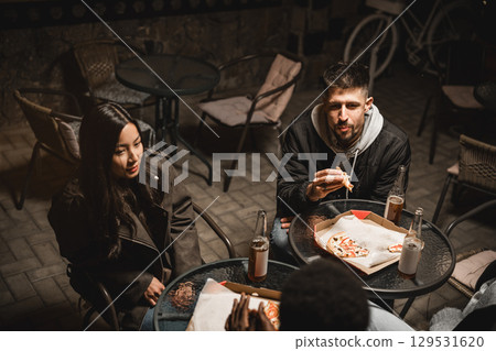 Friends enjoying late-night pizza and drinks at an outdoor cafe in a cozy atmosphere 129531620