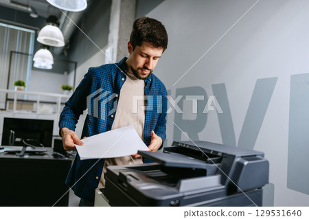 Man operating office printer while preparing documents in modern workspace during daytime Man operating office printer while preparing documents in modern workspace during daytime 129531640