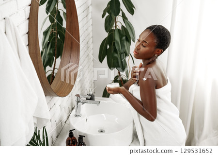 Woman applying moisturizer in a serene bathroom setting with plants and natural light Woman applying moisturizer in a serene bathroom setting with plants and natural light 129531652