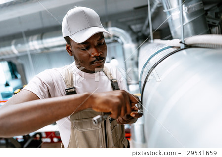 Man works on industrial pipe maintenance in a large workshop during the day 129531659