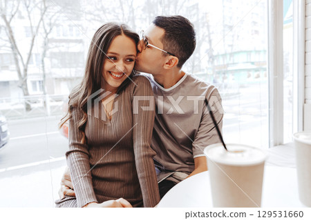 Couple enjoying a cozy moment at a cafe in a city, sharing smiles and affection during a leisurely afternoon 129531660