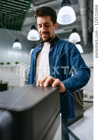 Man in a blue checkered shirt interacts with a modern workstation in a bright office during the day 129531666