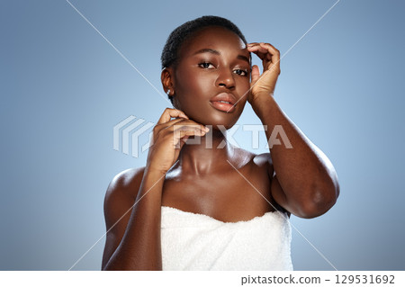 Model posing elegantly against a soft blue backdrop while wearing a towel, showcasing natural beauty and confidence in a studio setting 129531692