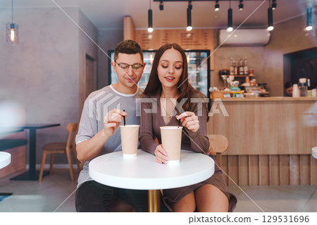 Young couple enjoying warm drinks at a cozy cafe in the afternoon, sharing a moment together in a welcoming atmosphere Young couple enjoying warm drinks at a cozy cafe in the afternoon, sharing a moment together in a welcoming atmosphere 129531696