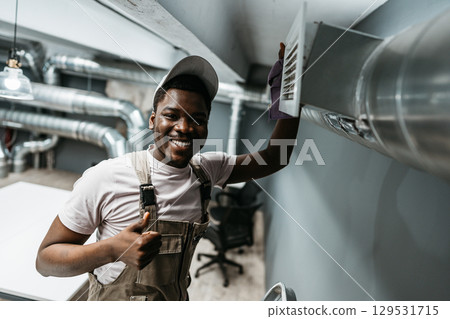Skilled worker performs maintenance on ventilation system in modern office space during daylight hours Skilled worker performs maintenance on ventilation system in modern office space during daylight hours 129531715