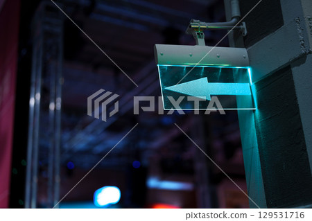 Directional sign illuminated in teal as it guides visitors in an indoor event space during nighttime activities Directional sign illuminated in teal as it guides visitors in an indoor event space during nighttime activities 129531716