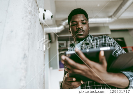 Man using tablet to monitor surveillance equipment in a modern office setting with a concrete wall and overhead lighting Man using tablet to monitor surveillance equipment in a modern office setting with a concrete wall and overhead lighting 129531717