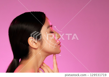 Woman demonstrating facial massage techniques with arrows indicating movement against a pink backdrop 129531719