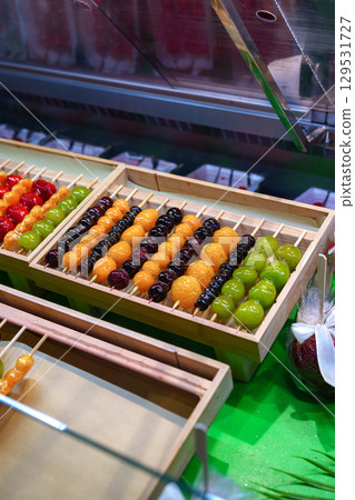 Colorful assortment of traditional sweet treats displayed in wooden trays at a market stall in evening light Colorful assortment of traditional sweet treats displayed in wooden trays at a market stall in evening light 129531727