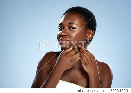 Young woman smiling and touching her chin against a light blue background while showcasing her skincare routine 129531803
