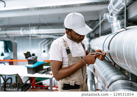 Young technician repairs ventilation system in modern workshop space during daylight hours 129531854