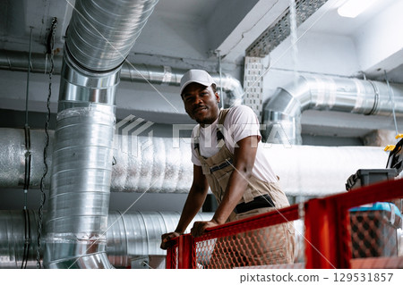 Worker on elevated platform inspecting ventilation system in industrial facility during daytime Worker on elevated platform inspecting ventilation system in industrial facility during daytime 129531857