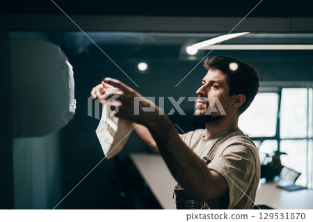 Man working on wall decoration indoors in a modern workspace during the day Man working on wall decoration indoors in a modern workspace during the day 129531870