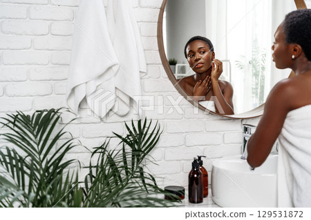 Woman applying skincare in a modern bathroom with green plants and natural light 129531872