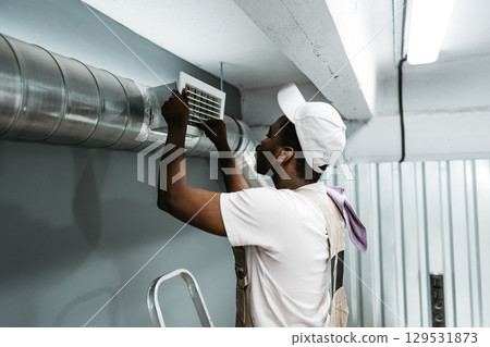 Worker repairs air vent in a commercial building during mid-morning hours of a busy weekday 129531873