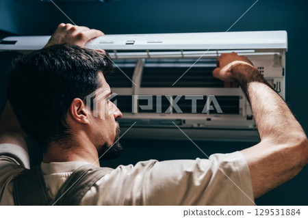 Technician performs maintenance on wall-mounted air conditioning unit in a modern room Technician performs maintenance on wall-mounted air conditioning unit in a modern room 129531884