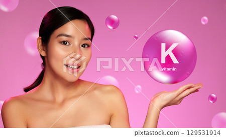 Woman showcasing vitamin K on her palm against a vibrant pink background with bubbles 129531914