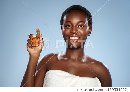 Smiling woman showcasing a perfume bottle against a soft blue background during a beauty presentation 129531922