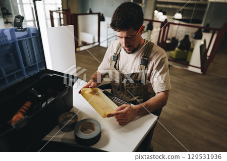 Man organizing tools and materials in a workshop while preparing for a crafting project in the afternoon light 129531936
