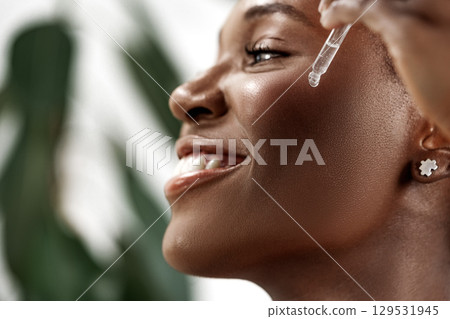 Smiling woman applying skin serum in a natural setting during daytime Smiling woman applying skin serum in a natural setting during daytime 129531945