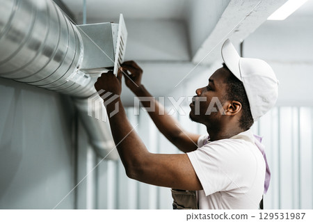 Young man repairs ventilation system inside a modern building during work hours Young man repairs ventilation system inside a modern building during work hours 129531987
