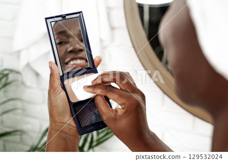 Woman applying makeup in bathroom mirror during morning routine for a fresh look at home 129532024