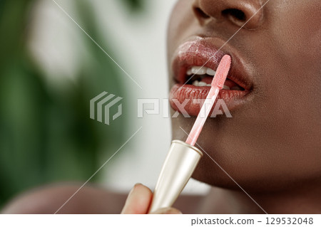 Lip gloss application by a person with dark skin tone in a bright, natural setting during daytime 129532048