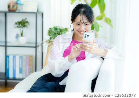 A young woman operating a smartphone in a room A young woman operating a smartphone in a room 129532077