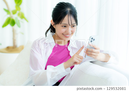 A young woman operating a smartphone in a room A young woman operating a smartphone in a room 129532081