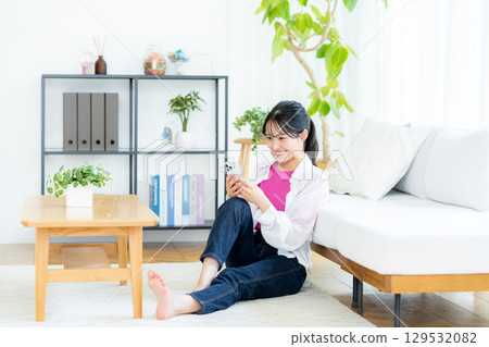 A young woman operating a smartphone in a room A young woman operating a smartphone in a room 129532082