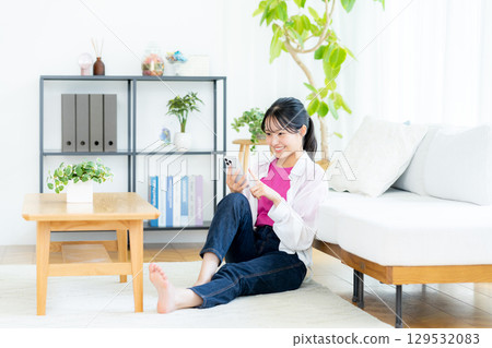 A young woman operating a smartphone in a room A young woman operating a smartphone in a room 129532083