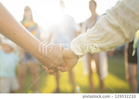 Two people holding hands in a field with friends in the background at sunset Two people holding hands in a field with friends in the background at sunset 129532210