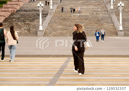 Young woman walking away, crossing street with large stone stairs background. Young woman walking away, crossing street with large stone stairs background. 129532337