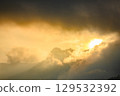 Golden light shines through the clouds and mountains. 129532392