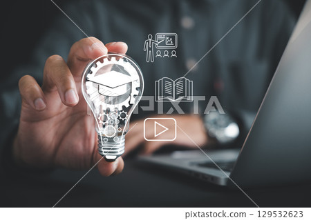 Learn e learning via technology, hand holds lightbulb filled with gears and graduation cap icon, teacher book and video icons float, and you can also learn from global creative experience displayed 129532623