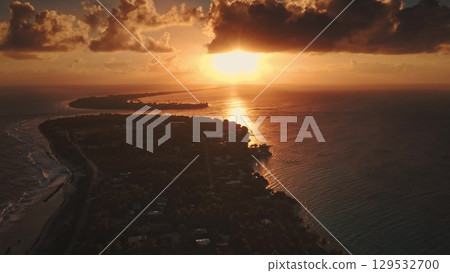 French Polynesia, Rangiroa island: bright sunset over a coastal city, casting warm hues across the water and illuminating the shoreline. Tranquil beauty of nature and urban life. Drone flight 129532700