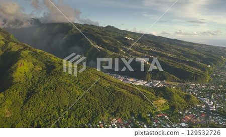Breathtaking scenery of Tahiti tropical island, French Polynesia. Lush green mountains canyon, green forest hills, houses, buildings, village cityscape under cloudy blue sky. Aerial drone panorama 129532726