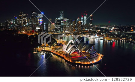 Australia, Sydney New South Wales: Sydney Opera House and city skyline at night, reflecting bright lights on water harbor surface, creating a breathtaking cityscape panorama. Aerial view drone Australia, Sydney New South Wales: Sydney Opera House and city skyline at night, reflecting bright lights on water harbor surface, creating a breathtaking cityscape panorama. Aerial view drone 129532729