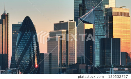United Kingdom, London: Warm sunset light illuminating the modern skyscrapers of London's financial district, including 30 St Mary Axe (The Gherkin), creating a stunning cityscape. Drone flight footag 129532737