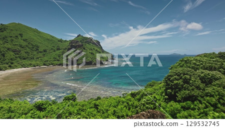 Aerial drone view of the amazing beach landscape of Kuata island in Fiji featuring lush tropical vegetation covering the hills, turquoise water, and a beautiful sunny day. Drone flight 129532745