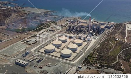 Cyprus: Aerial view of Vasilikos Power Station emitting smoke from its chimney near the sea in Cyprus, showing fuel storage tanks and industrial buildings. Drone flight Cyprus: Aerial view of Vasilikos Power Station emitting smoke from its chimney near the sea in Cyprus, showing fuel storage tanks and industrial buildings. Drone flight 129532766