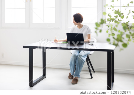A woman working on a laptop and notebook in a bright room 129532974