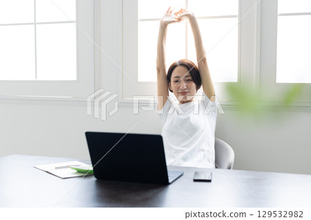 一位女士在辦公桌前工作時伸展雙臂 129532982