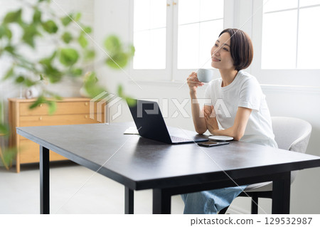 微笑的女人在辦公桌前放鬆，手裡拿著咖啡杯 129532987