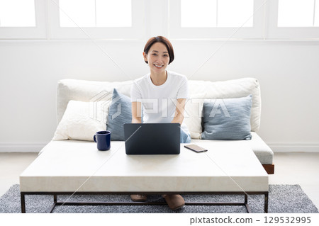 A smiling woman working on a laptop in a bright living room 129532995