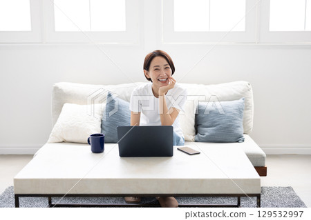 一位微笑的女士在明亮的客廳裡用筆記型電腦工作 129532997