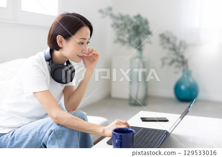 一位女士戴著耳機,坐在沙發上使用筆記型電腦 一位女士戴著耳機,坐在沙發上使用筆記型電腦 129533016