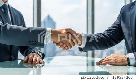 Closeup of two businessmen shaking hands in modern office with city view, concept of successful partnership, deal, and corporate agreement Closeup of two businessmen shaking hands in modern office with city view, concept of successful partnership, deal, and corporate agreement 129534203
