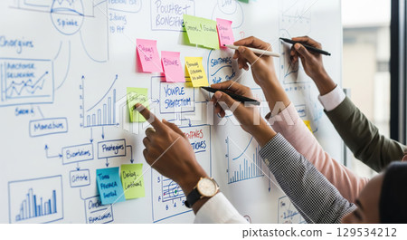 Close up of business team brainstorming on whiteboard, colleagues collaborating on project strategy using sticky notes and drawing charts in office meeting Close up of business team brainstorming on whiteboard, colleagues collaborating on project strategy using sticky notes and drawing charts in office meeting 129534212