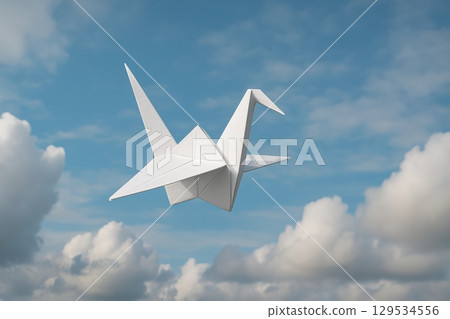 White origami crane flying in a blue sky with clouds, symbolizing peace, remembrance 129534556